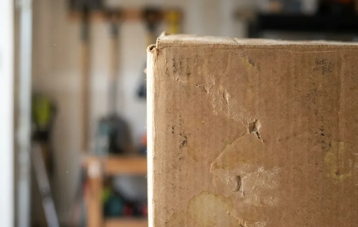 Cardboard boxes stacked against the wall of a garage with tools racked behind Cardboard boxes stacked against the wall of a garage with tools racked behind